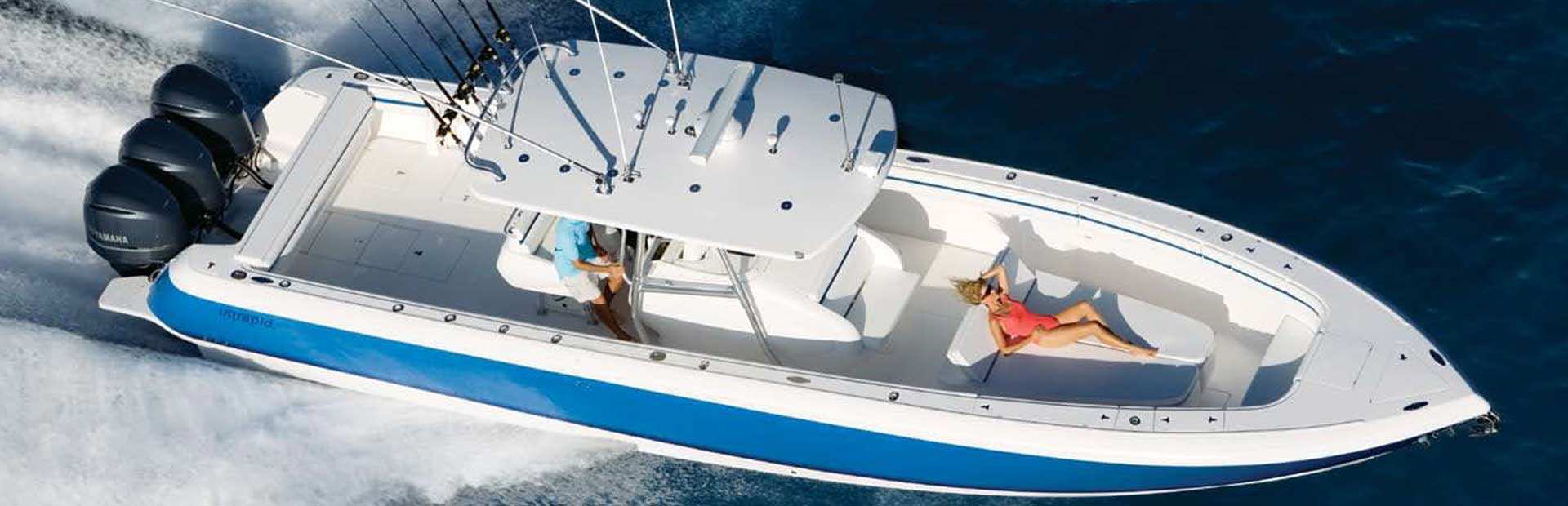 Sport fishing boat at high speed while a woman lounges on lounge chair in the bow.