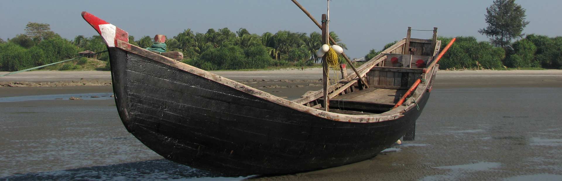 Old wooden fishing boat sitting on sand at low tide by the shore.